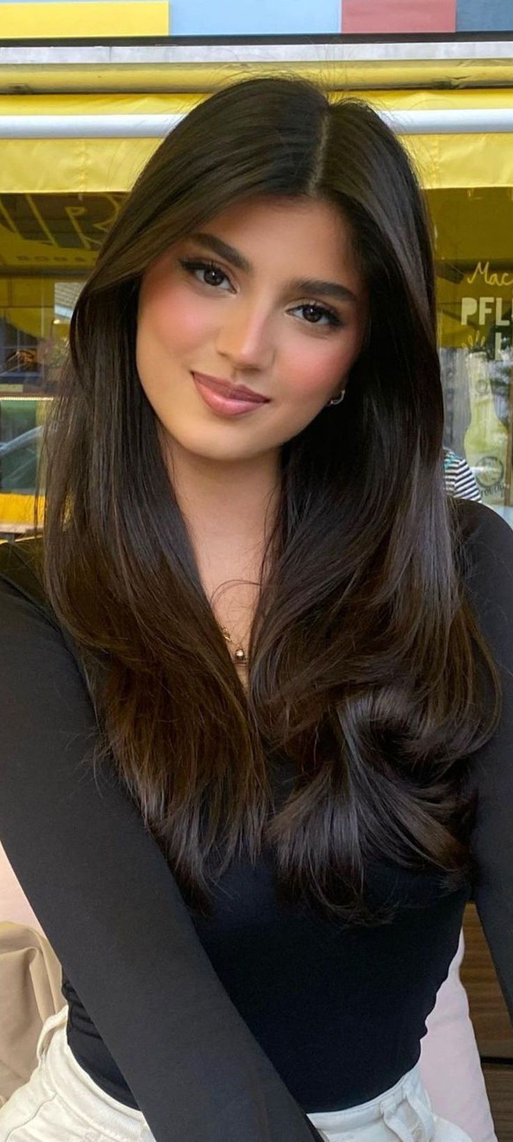 Woman with long dark hair wearing a black top and necklace indoors