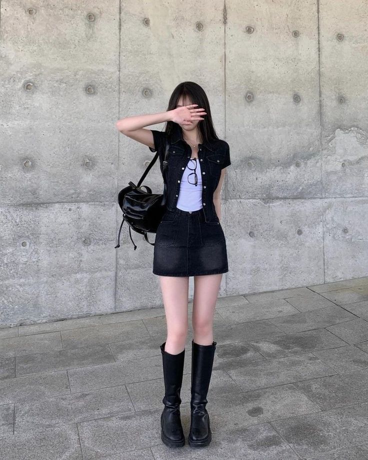 Woman in a black denim jacket and mini skirt with a backpack covering her face