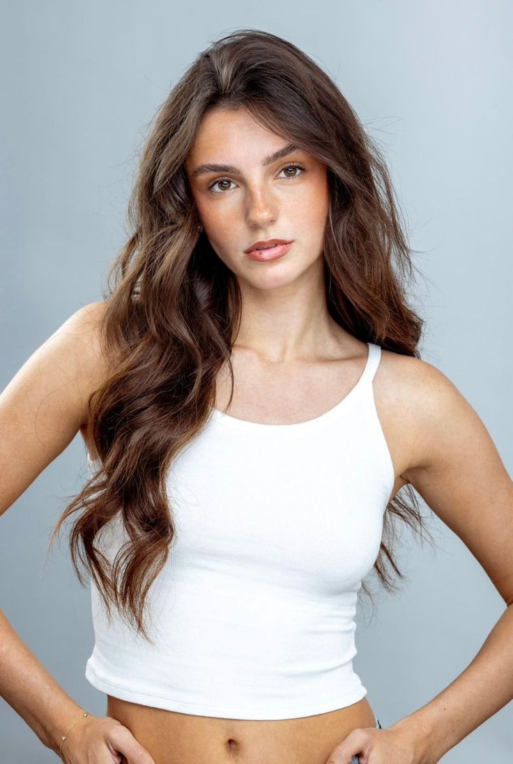 Woman with long brown hair and freckles wearing a white tank top