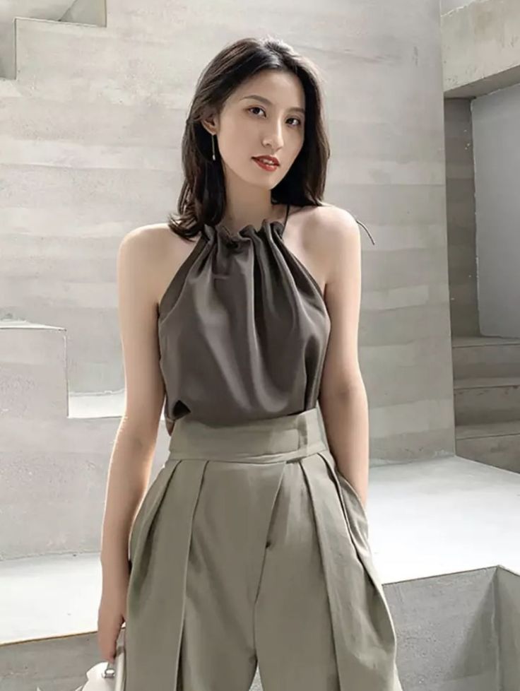 Woman in a dark halter top and pleated pants indoors