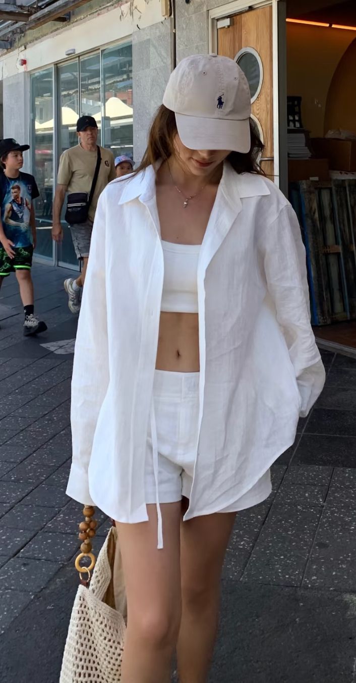 Woman in a white crop top, shorts, and baseball cap on a street