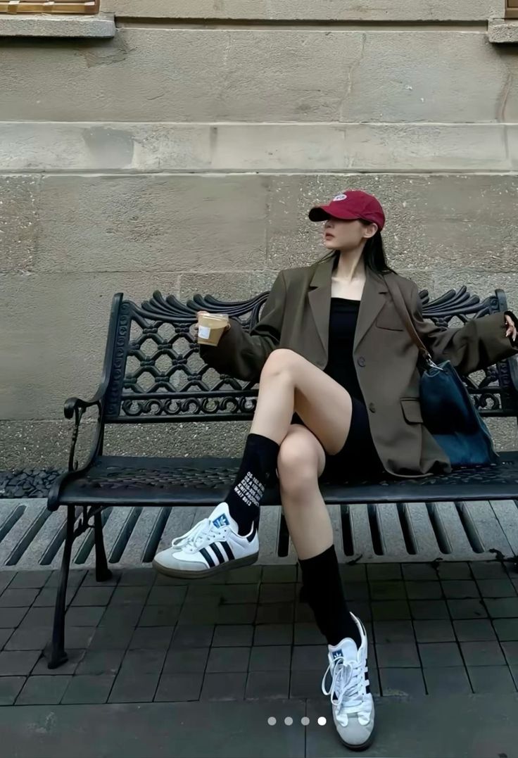 Woman in a red cap and oversized blazer sitting on a bench outdoors