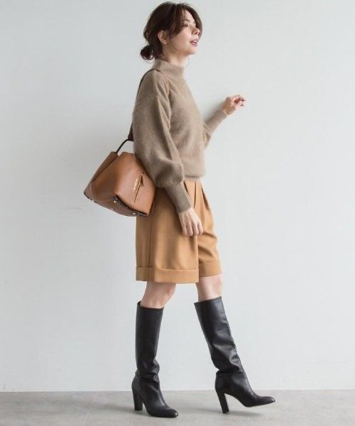 Woman in a brown sweater, bermuda shorts, and knee-high boots with a brown handbag