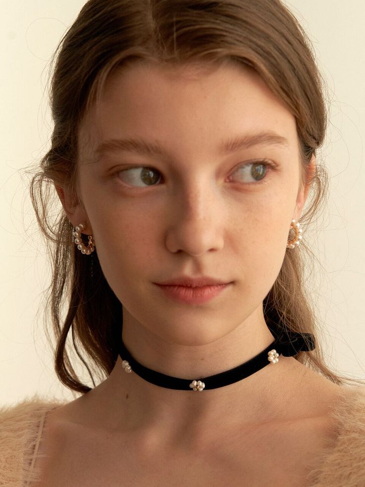 Young woman with long brown hair wearing a black velvet choker and pearl earrings