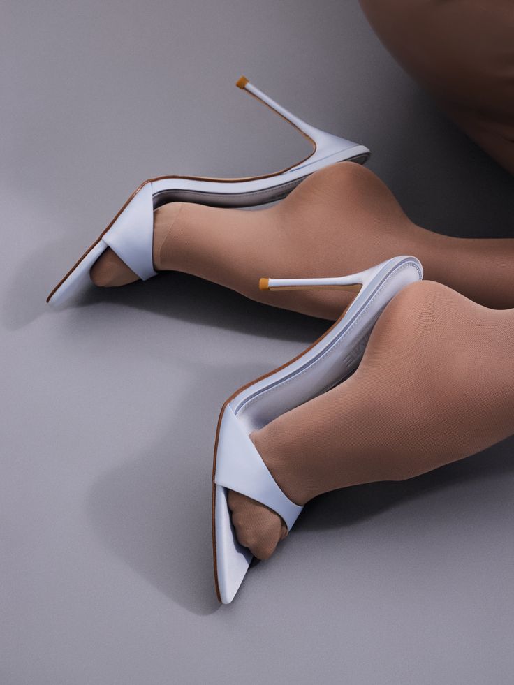 Legs in nude tights and light blue high heels on a gray background