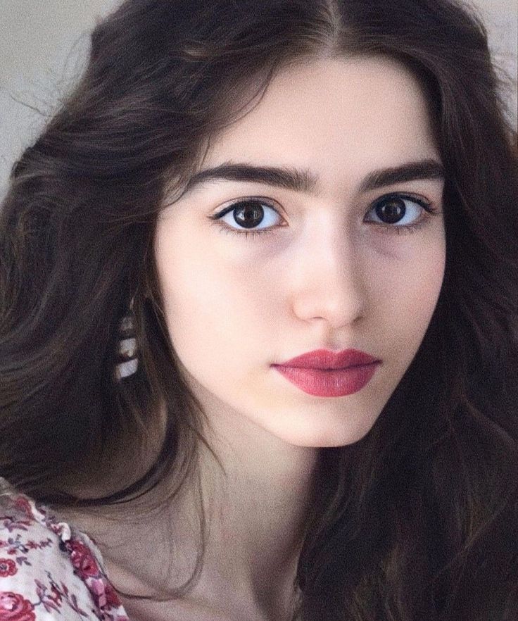 Woman with long dark hair and pink lipstick wearing a floral top