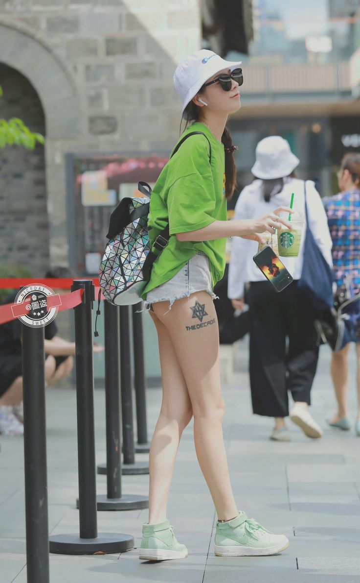 Woman in a green t-shirt and denim shorts with a leg tattoo on a street