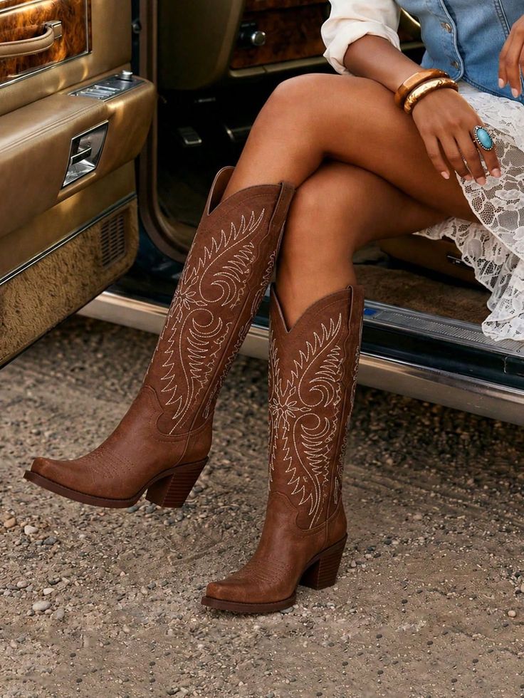 Woman in cowboy boots and a lace dress sitting in a car with legs crossed
