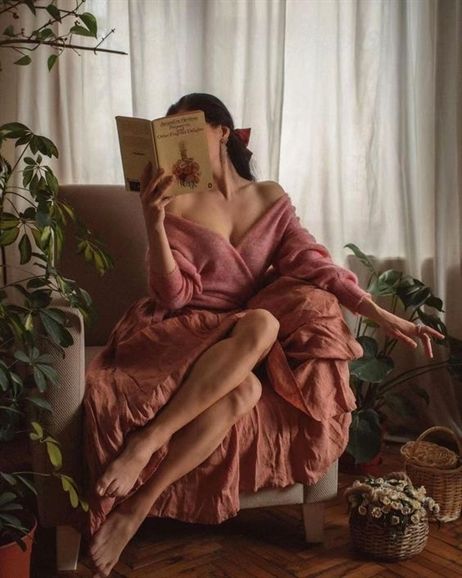 Woman in a pink dress reading a book indoors with plants