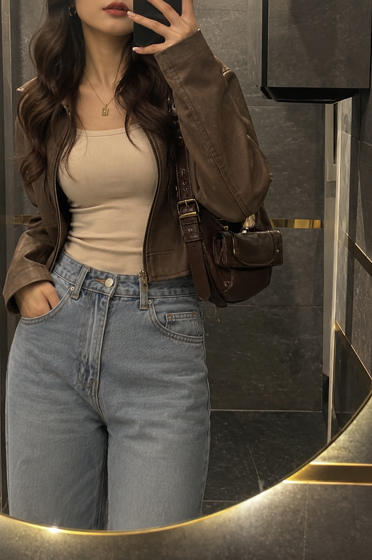 Woman in a brown jacket and blue jeans taking a mirror selfie