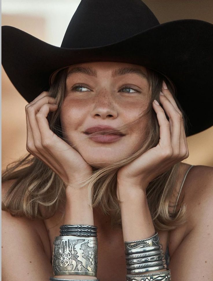 Woman with freckles and a cowboy hat, wearing silver bracelets and looking to the side
