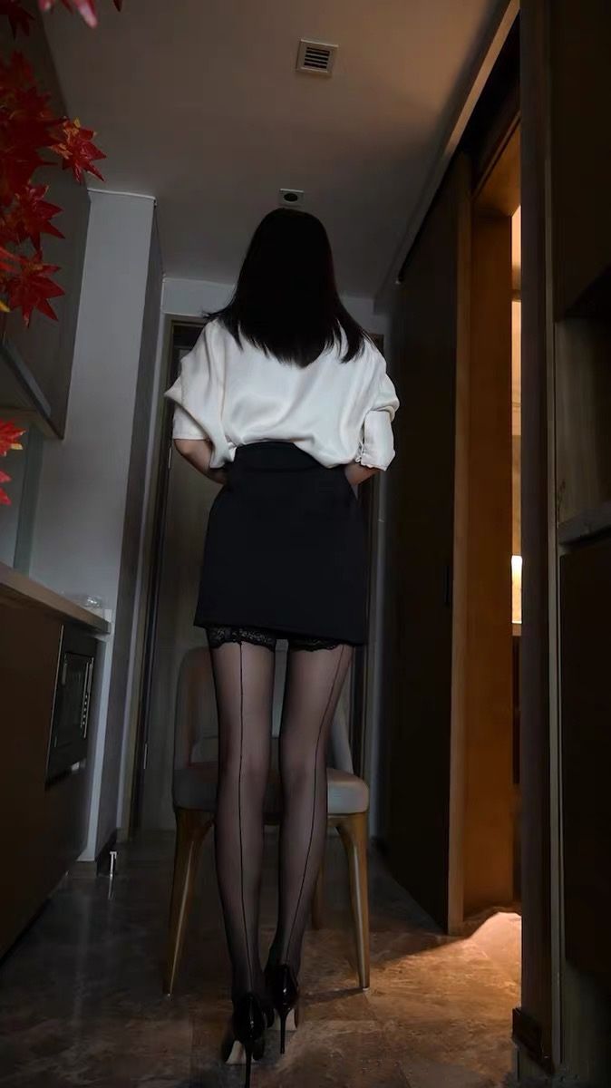 Woman in a white shirt, black skirt, and stockings from behind indoors