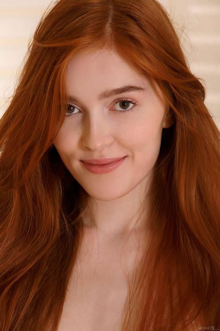 Woman with long red hair smiling at the camera with soft lighting