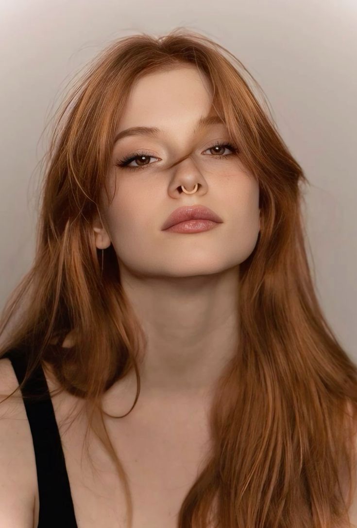 Woman with long red hair and a septum ring looking directly at the viewer