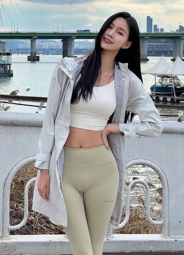 Woman in a white crop top and light green leggings by a river with a bridge in the background