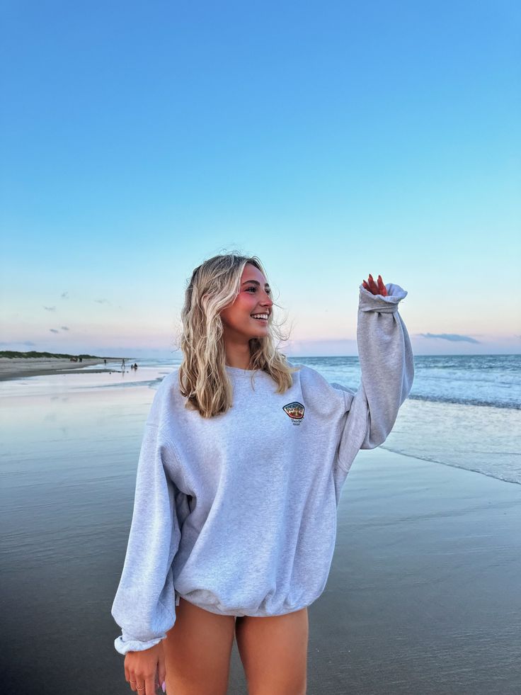 Woman with long blonde hair in an oversized sweatshirt on a beach at sunset
