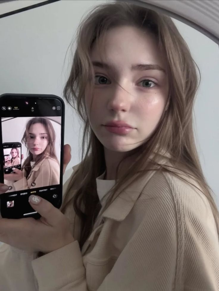 Woman with long hair holding a phone to take a mirror selfie