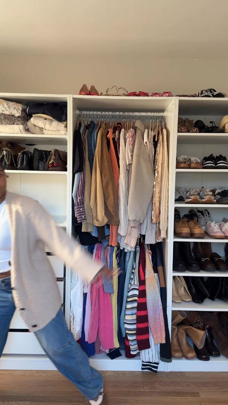 Person in a cardigan and jeans in front of a closet with clothes and shoes