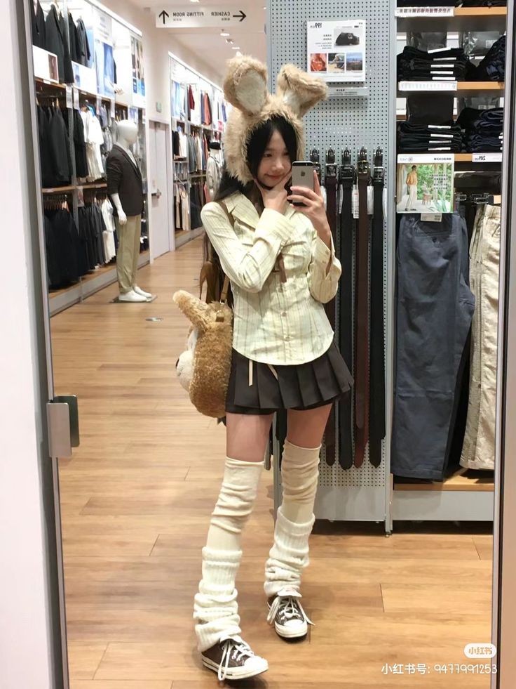Young woman in a bunny hat and pleated skirt taking a mirror selfie in a store