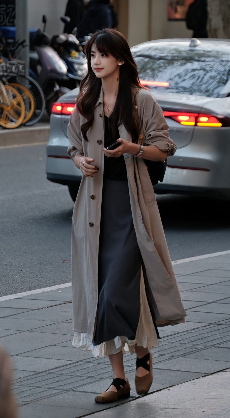 Woman with long hair wearing a trench coat and long skirt on a city street