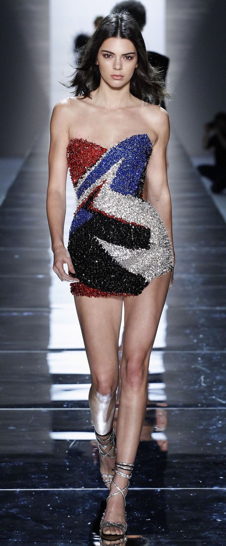 Woman in a sequined strapless dress walking on a runway