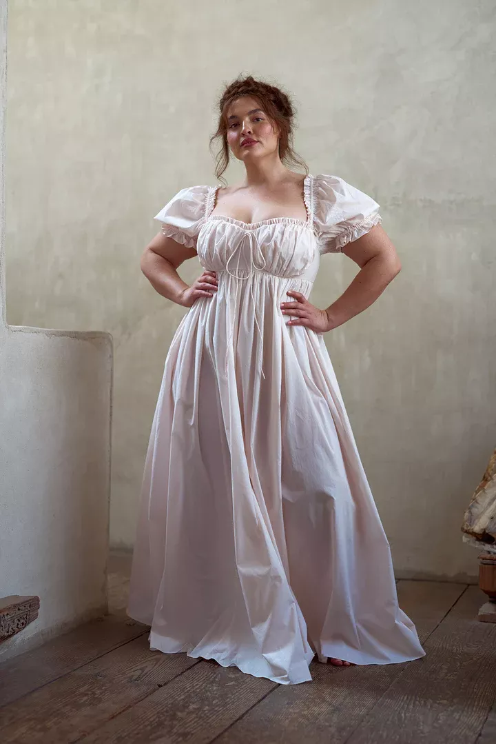 Woman in a long light-colored dress with puffy sleeves standing indoors