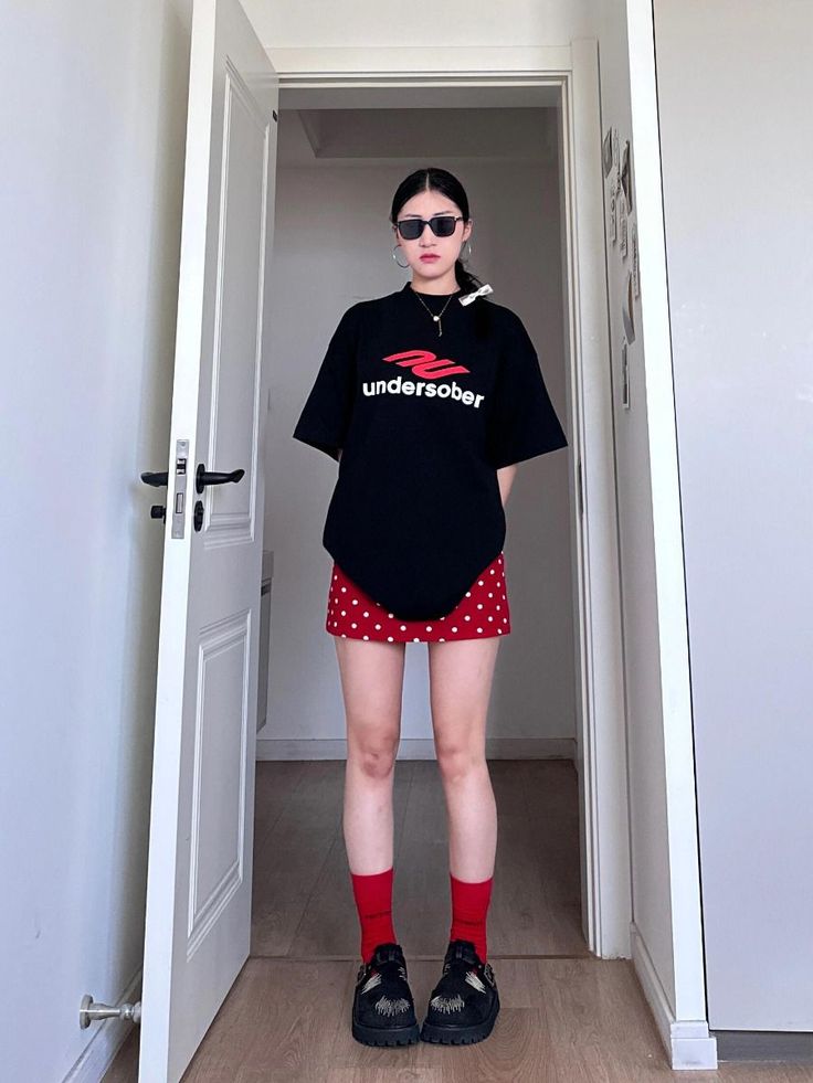 Woman in a black t-shirt and red polka dot skirt standing in a doorway