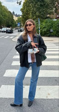 Woman in a leather jacket and jeans standing on a street with coffee