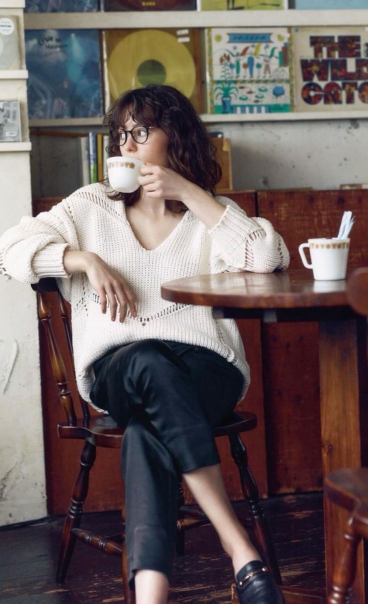 Woman with curly hair and glasses drinking coffee in a cafe