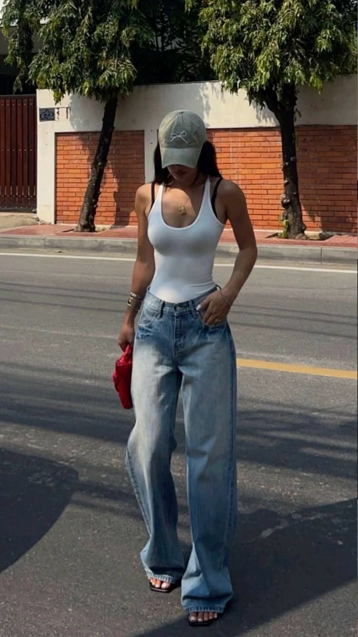 Woman in a white tank top, baggy jeans, and a baseball cap on a street