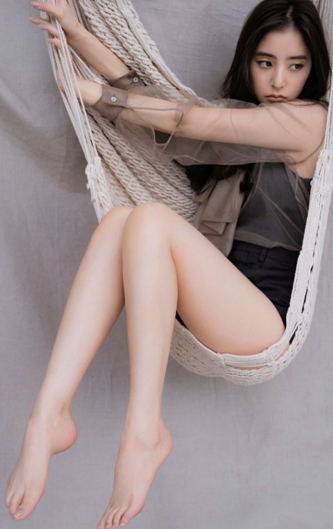 Woman with long black hair sitting in a hammock wearing a sheer top and shorts