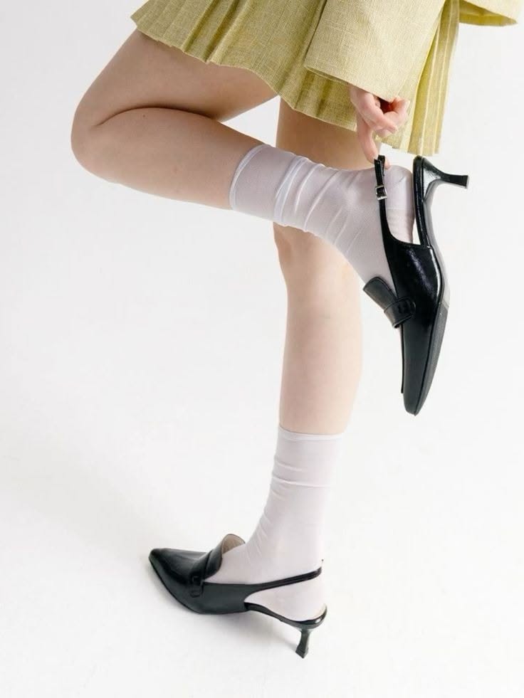 Person wearing white socks and black heels with a pleated skirt