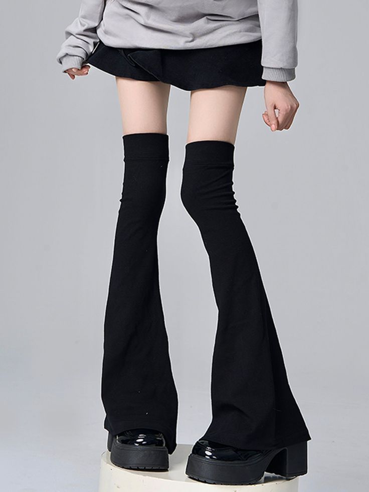 Person in a black skirt, gray hoodie, and black leg warmers with platform shoes