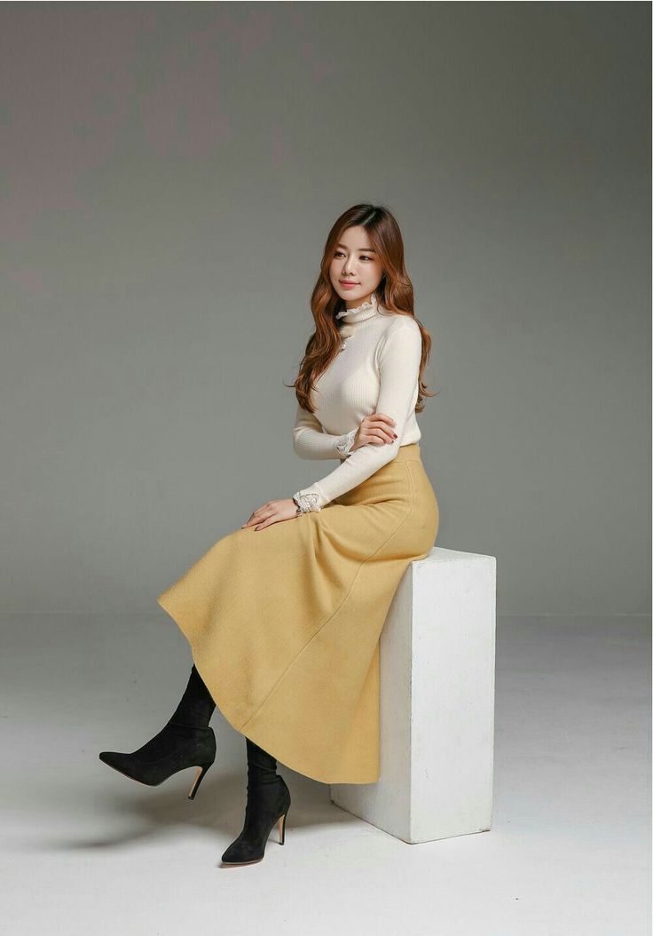 Woman in a cream turtleneck and yellow long skirt sitting on a white block