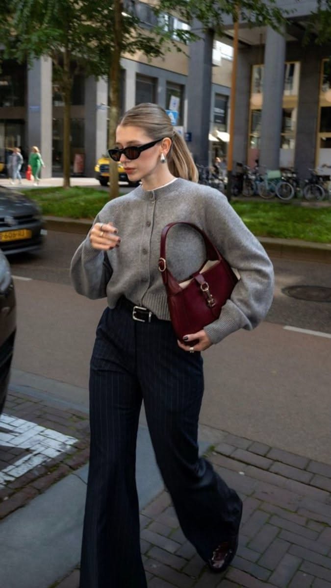 Woman in a gray cardigan and pinstripe pants walking on a city street