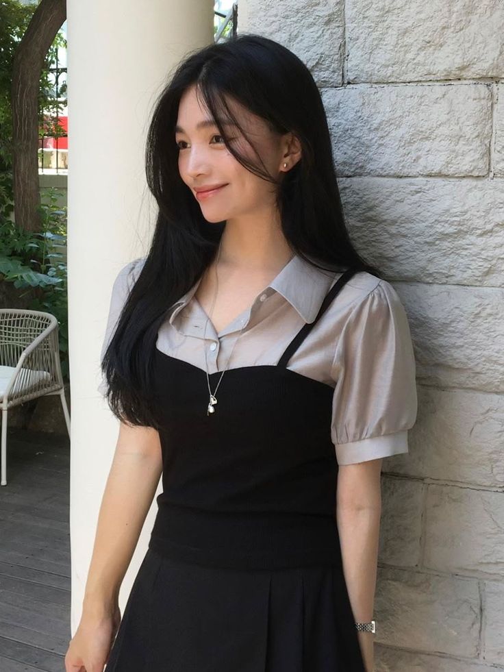 Woman with long black hair wearing a collared shirt and black top outdoors