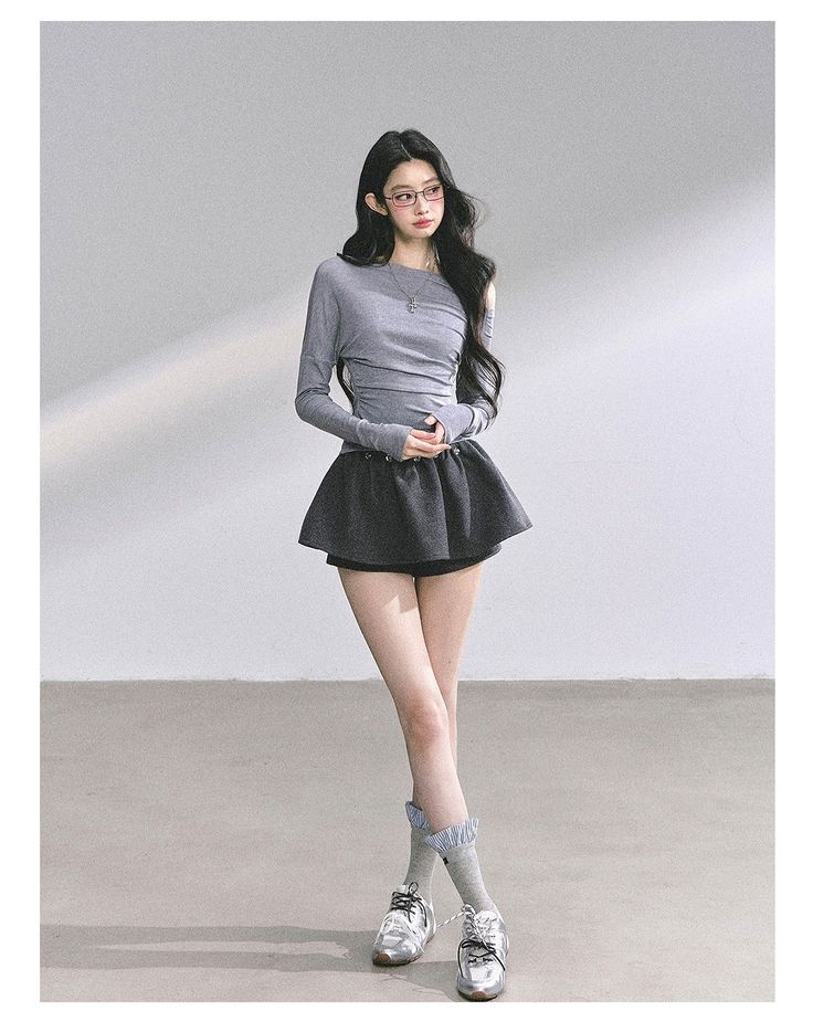Woman with long black hair and glasses wearing an off-shoulder top and mini skirt