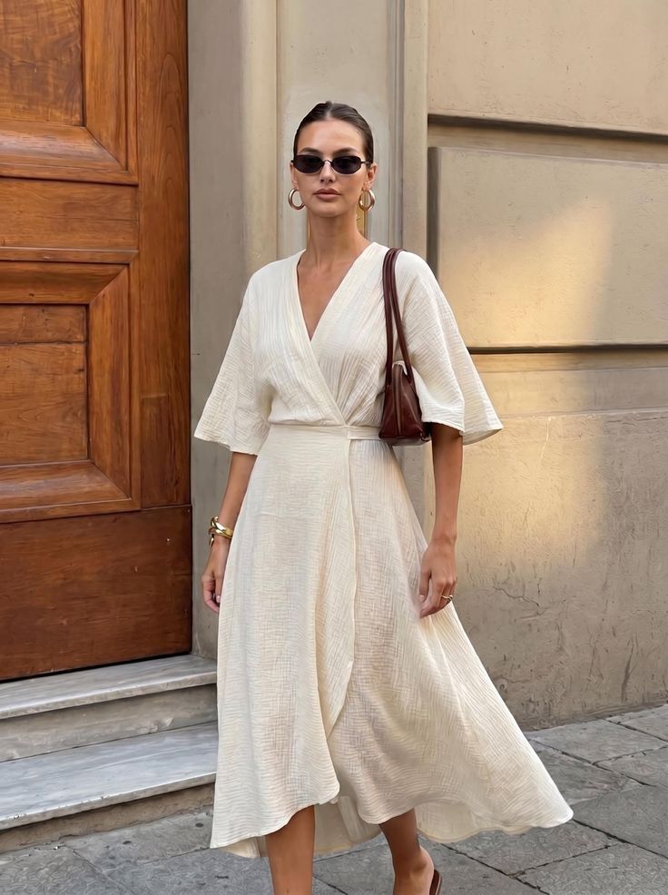 Woman in a cream wrap dress and sunglasses standing outdoors