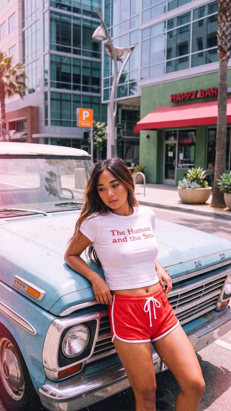 Woman in a white crop top and red shorts leaning on a vintage blue truck