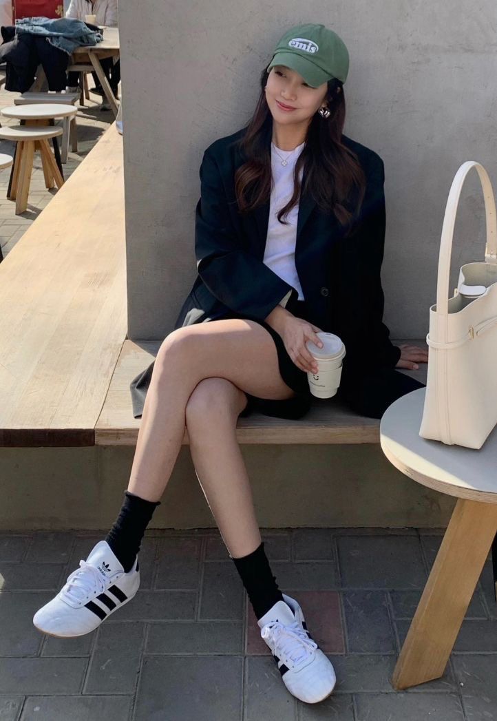 Woman in a green cap and black blazer sitting on a bench outdoors