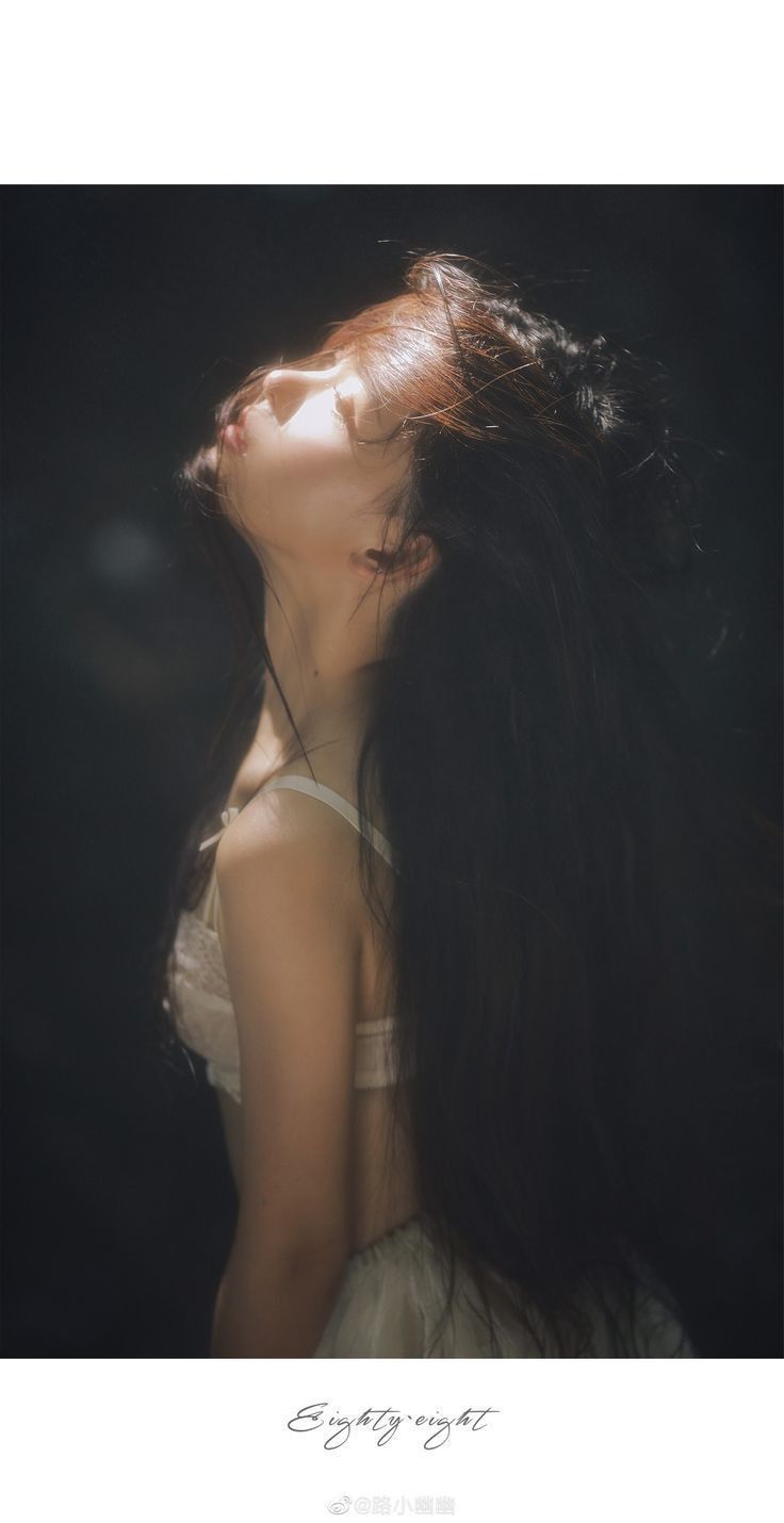 Woman with long hair looking up into soft light against a dark background