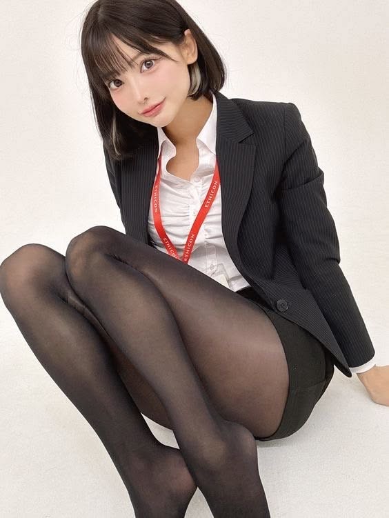 Woman in a black blazer and tights with a red lanyard, sitting on the floor
