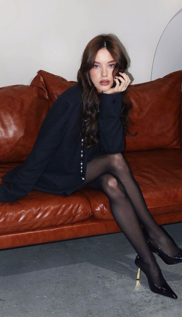 Woman with long brown hair wearing a black cardigan and tights on a brown couch