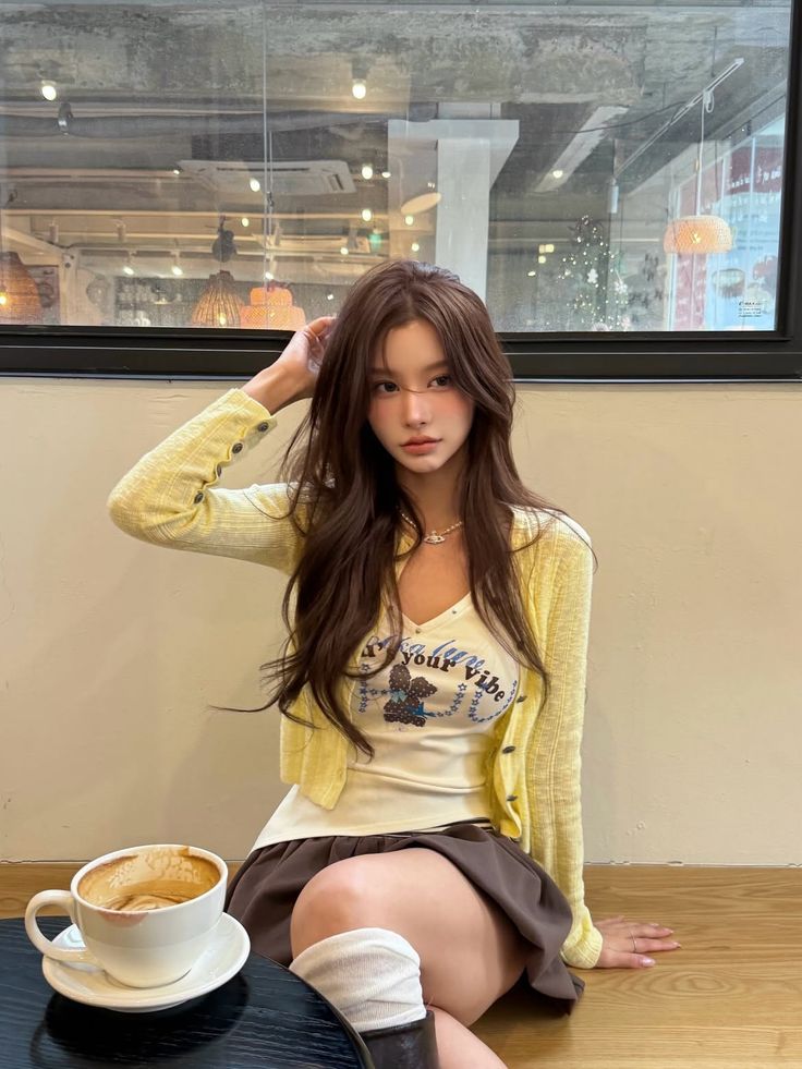Woman with long brown hair wearing a yellow cardigan and mini skirt in a cafe