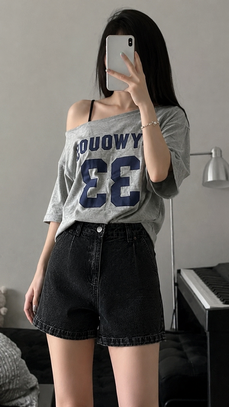 Person in a gray off-shoulder top and black denim shorts taking a mirror selfie