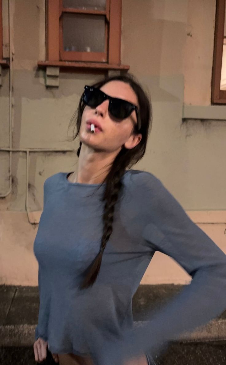 Woman with a cigarette and sunglasses wearing a blue top outdoors at night