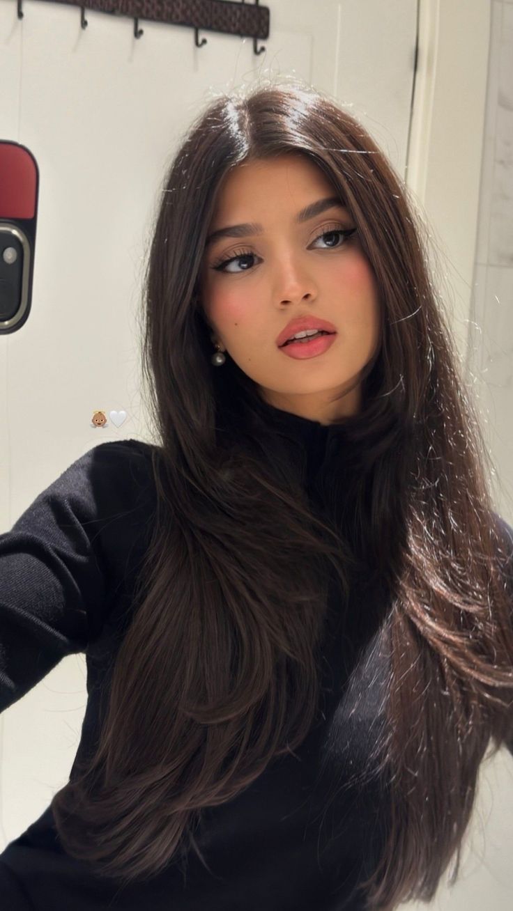 Woman with long dark hair wearing a black top and pearl earrings