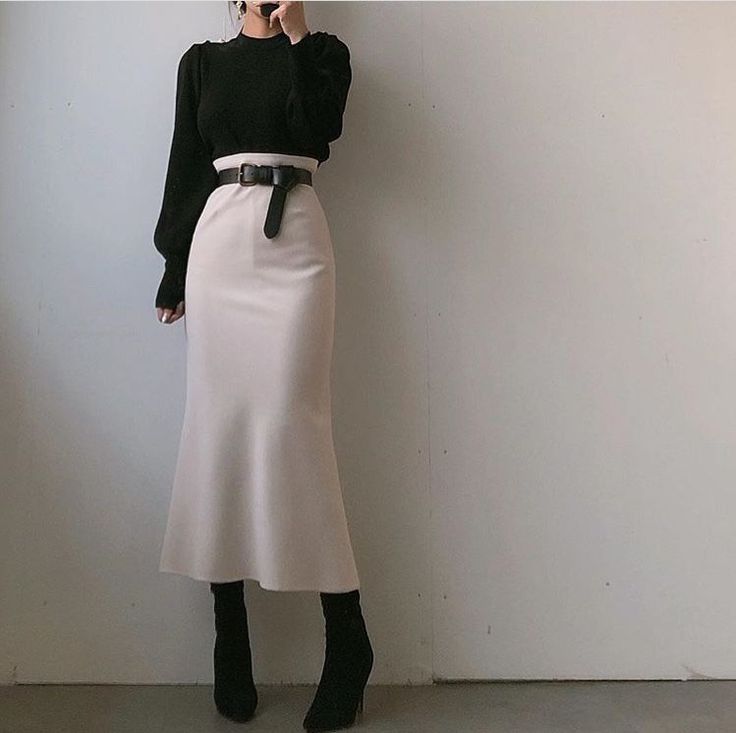 Person in a black sweater and midi skirt with a black belt and boots