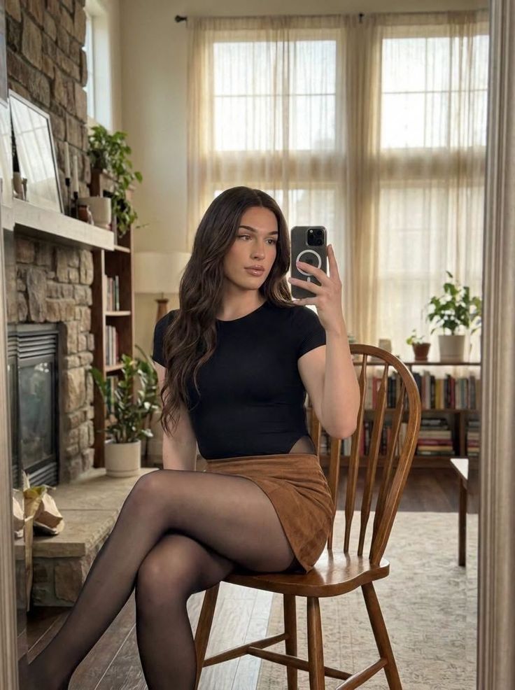 Woman with long brown hair taking a mirror selfie while sitting indoors