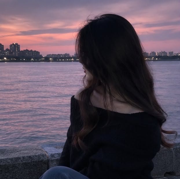 Woman with long hair looking at a sunset over a city waterfront